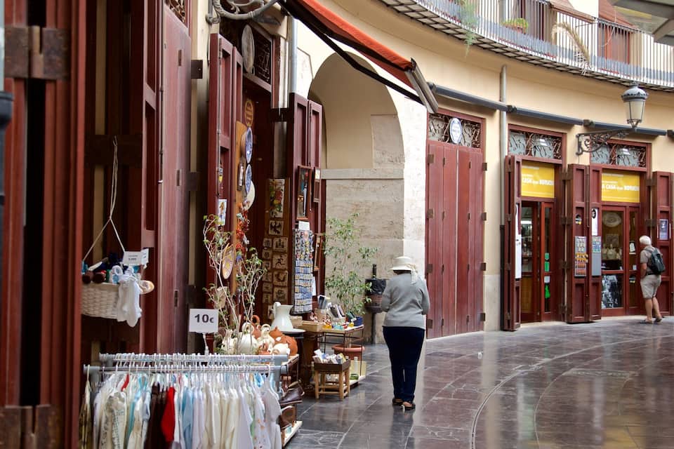 Rua com lojas, uma mulher comprando e um homem caminhando.