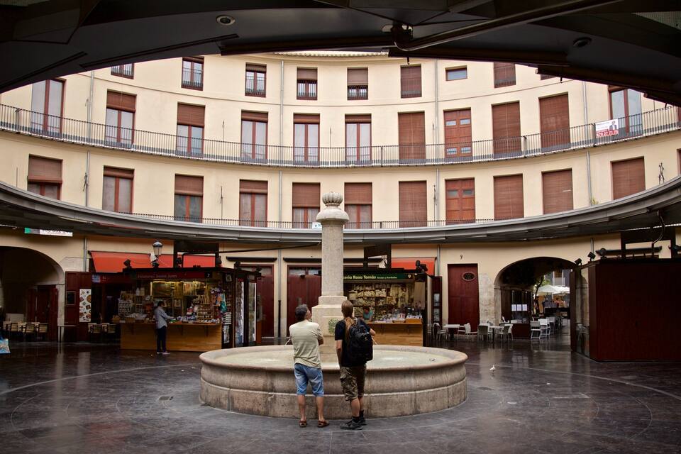 Una plaza circular con una fuente central, rodeada de edificios de varios pisos con balcones y tiendas.