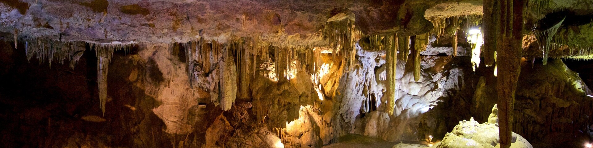 Una cueva con estalactitas y estalagmitas, iluminada por luces artificiales.