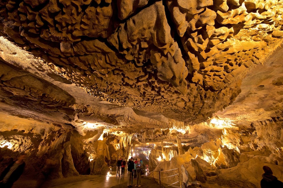 A cave with stalactites and stalagmites, illuminated by artificial lighting.