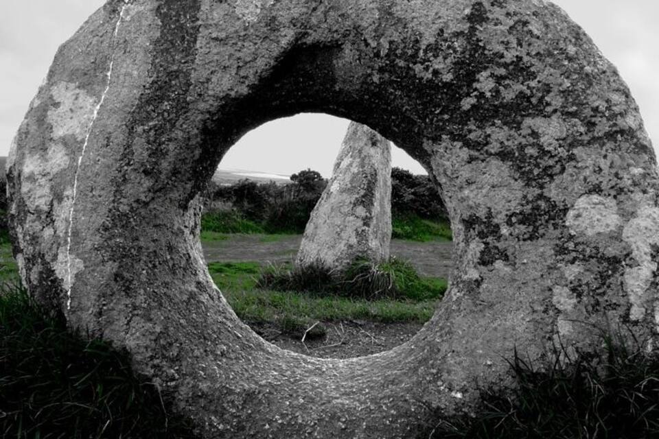 A large stone ring with a circular opening, surrounded by grass and other stones.