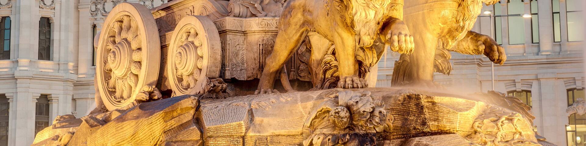 A detailed fountain sculpture with a seated figure and lions, set against a grand building with ornate architecture.