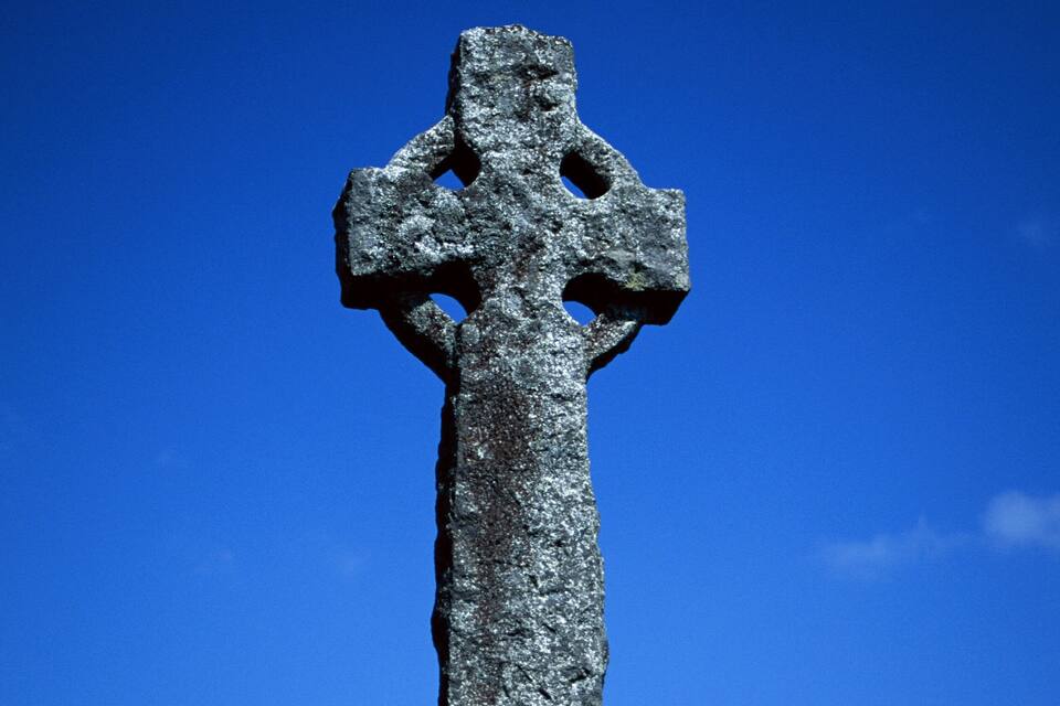 A standing stone cross against a clear blue sky.