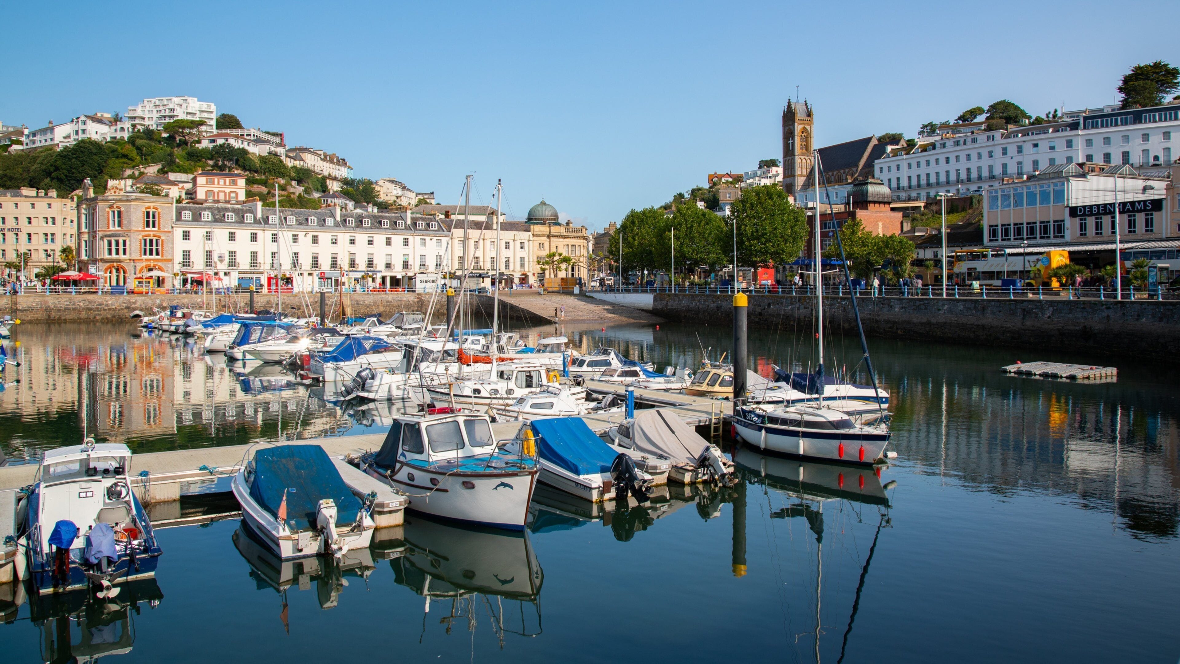 A marina with various boats docked, a prominent church tower, and historic buildings along the waterfront.