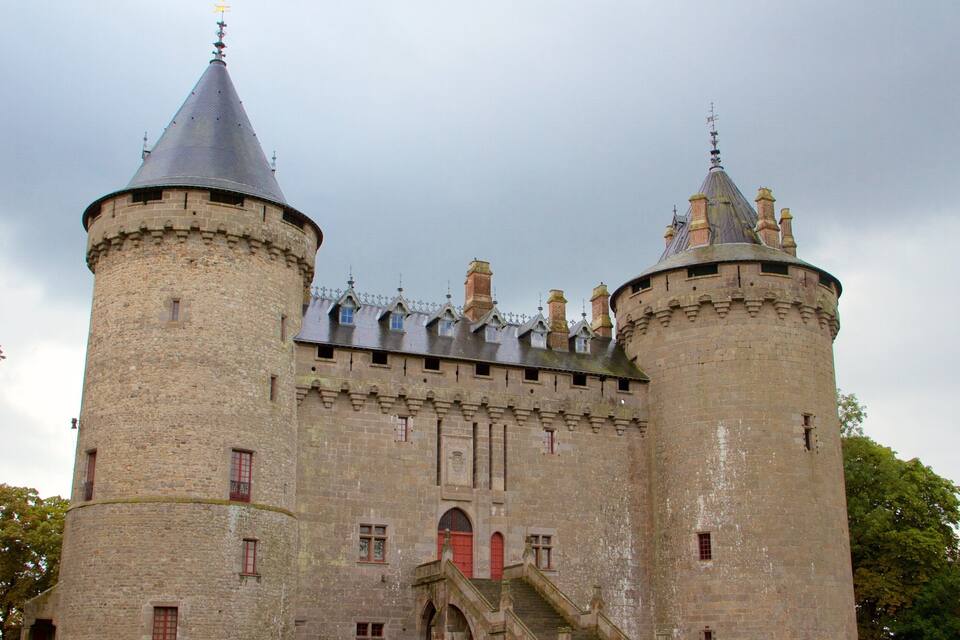 Um castelo histórico com duas torres imponentes, uma entrada central e um fosso ao redor.