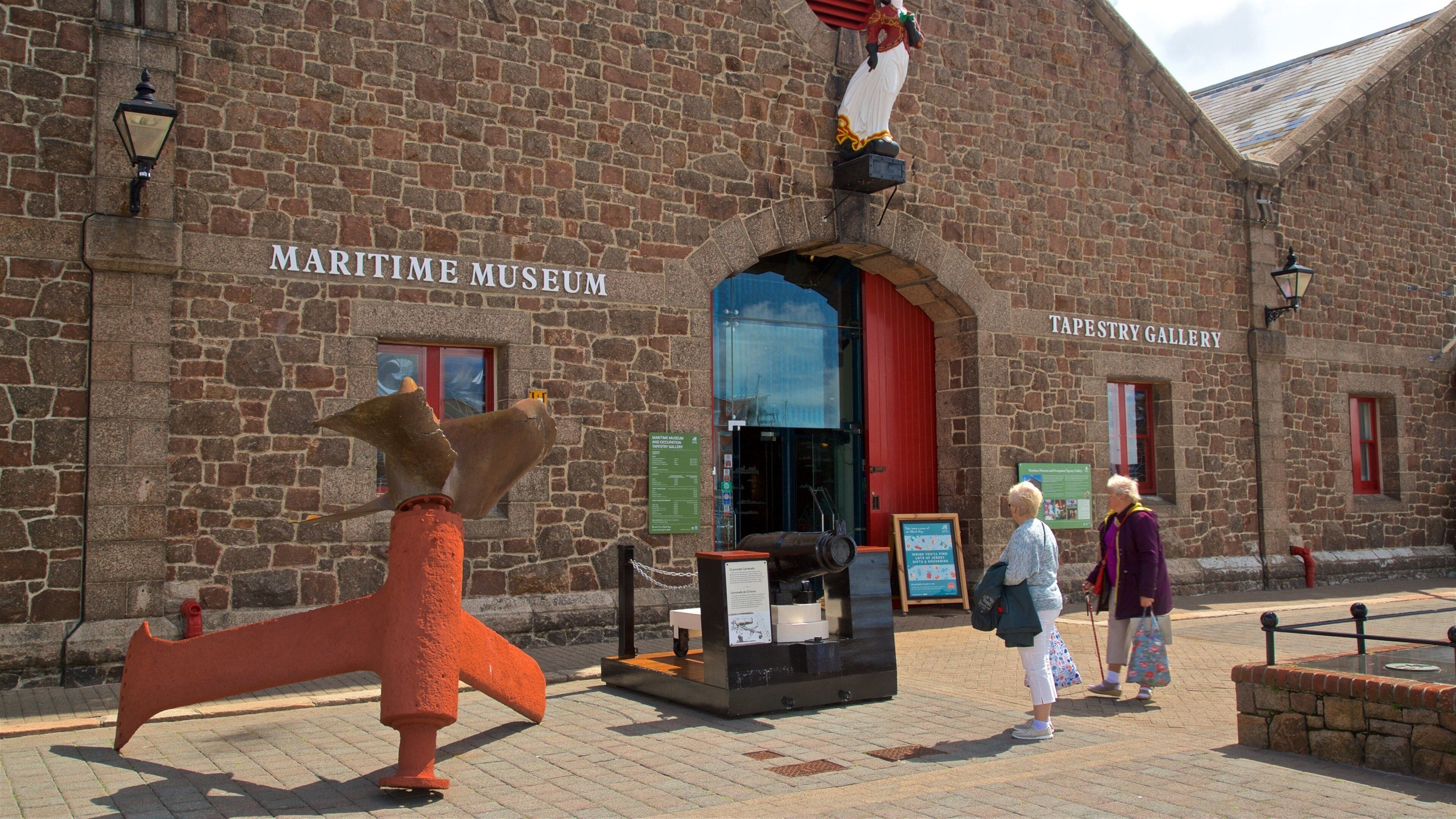 El Museo Marítimo y la Galería de Tapices, con un gran timón de barco y una estatua de una figura con un abrigo rojo.