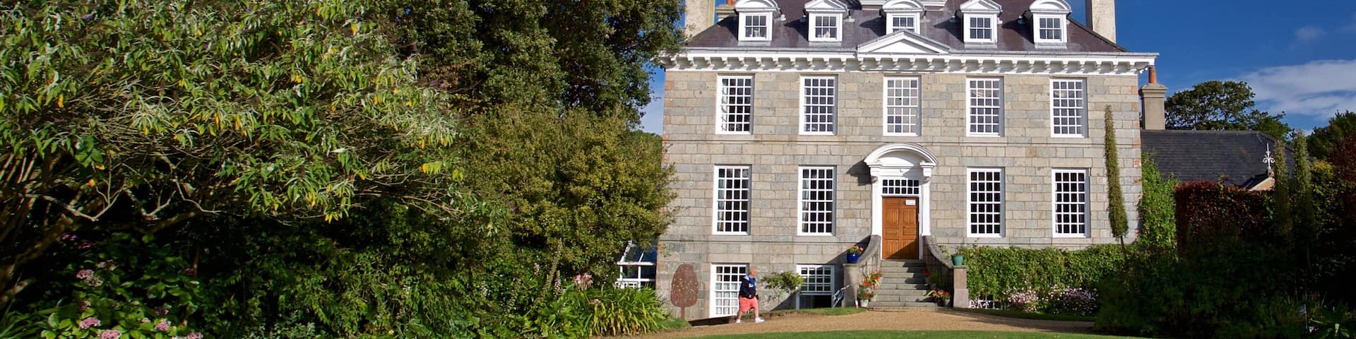 A large stone building with a symmetrical facade, a central entrance, and a well-maintained lawn.