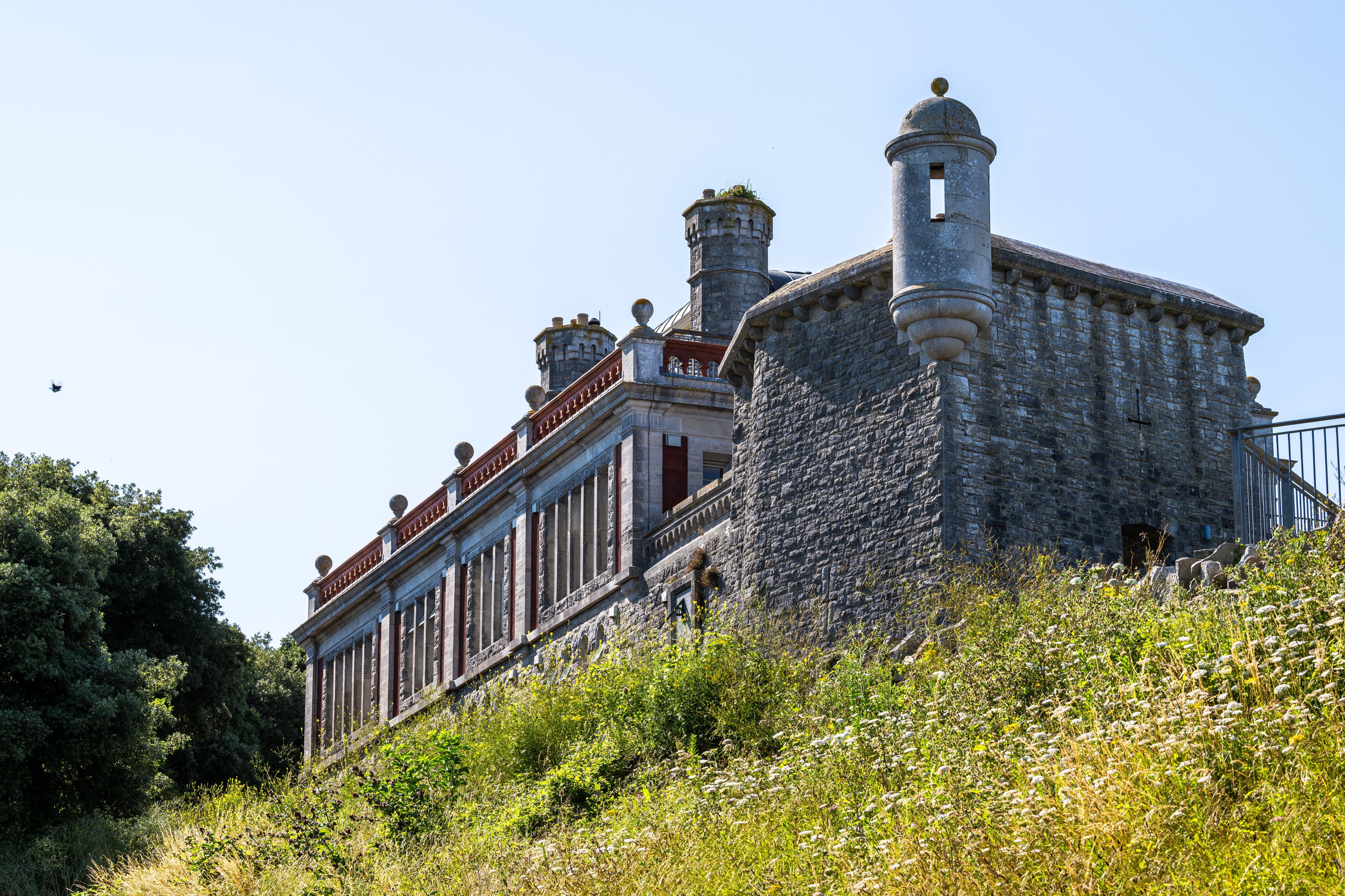 A historic stone building with two towers, surrounded by lush greenery.
