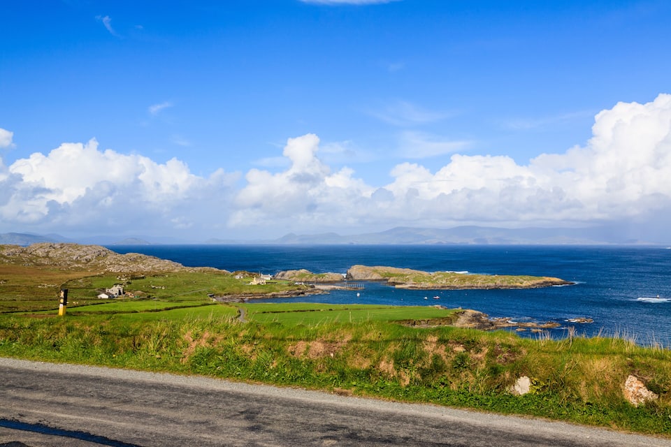 A coastal landscape with green fields, rocky outcrops, and a clear blue sky.