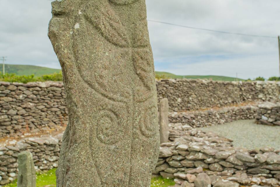 A stone monument with carvings, surrounded by a stone wall and a grassy landscape.