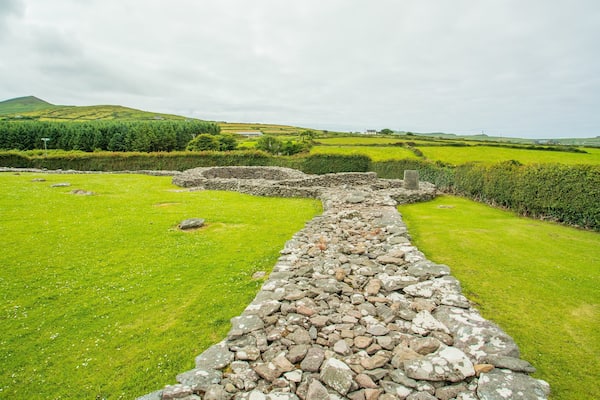 A stone wall leading through a green field with a hill in the background.