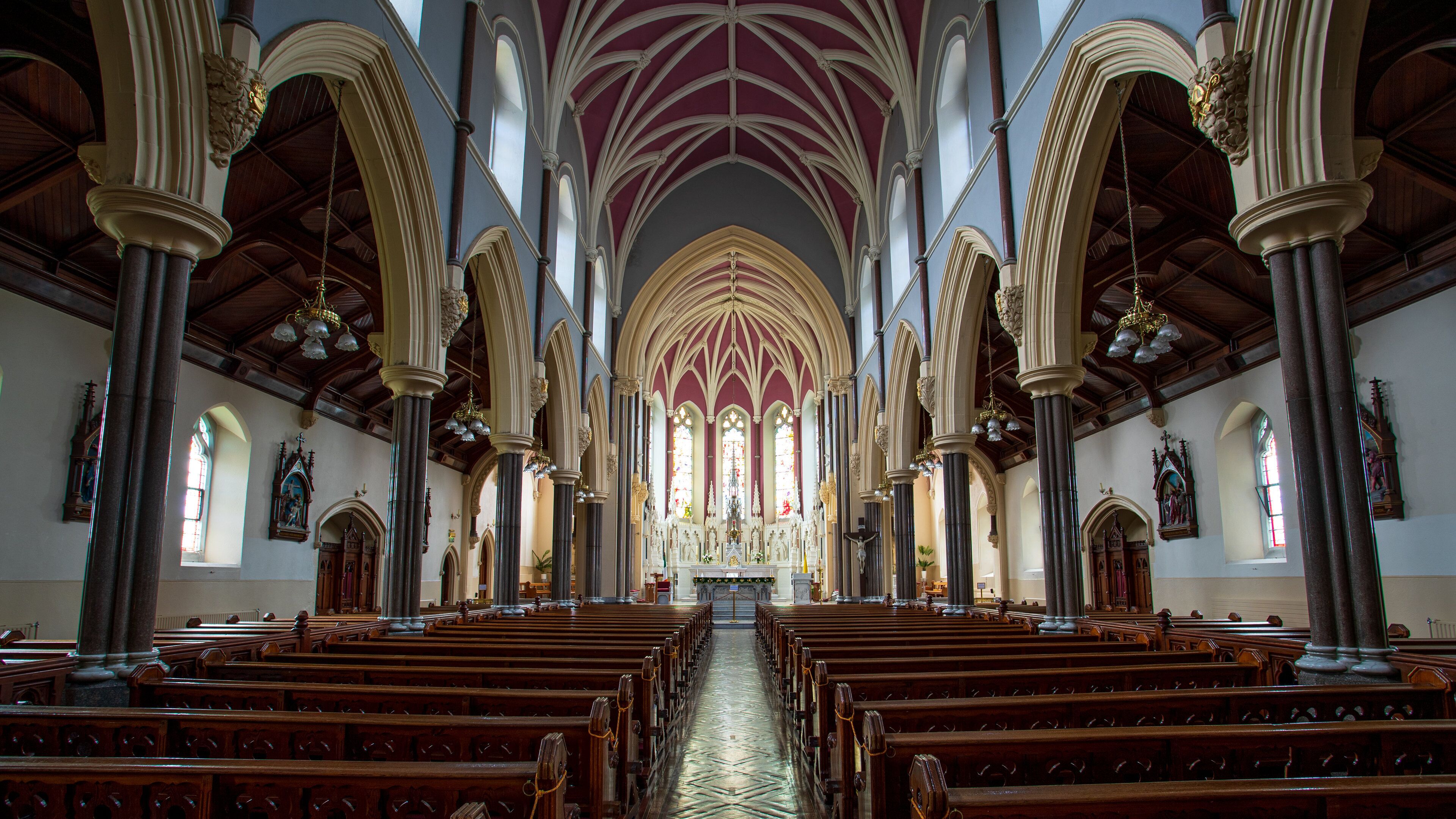 Ein Kircheninneres mit gewölbter Decke, Holzbänken und Buntglasfenstern.