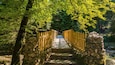 A wooden bridge with stone walls on either side, surrounded by lush green trees.