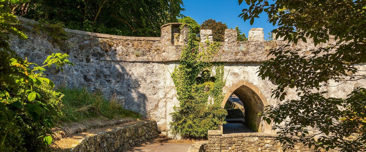 A stone bridge with an arched passageway, surrounded by lush greenery and a stone wall.