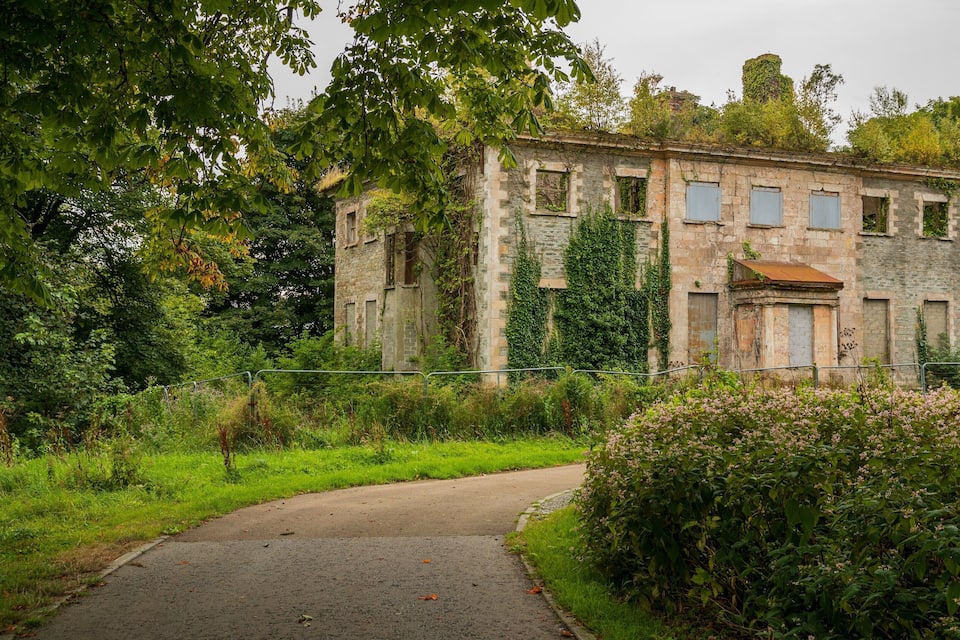 Un vieux bâtiment en pierre, entouré d’une végétation luxuriante et bordé d’un chemin pavé.