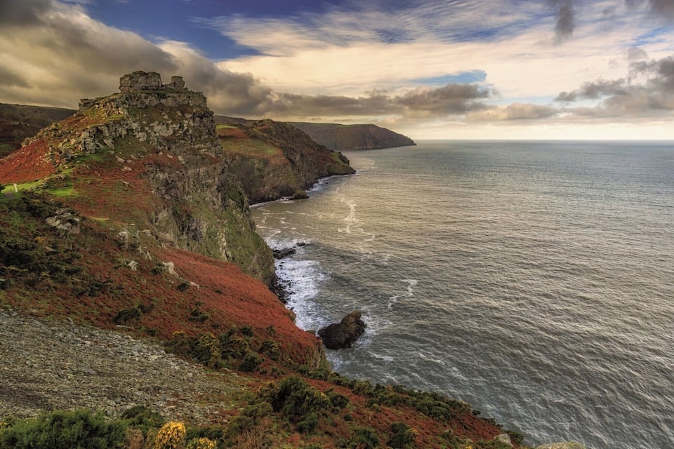 A coastal landscape with a rocky cliff and a ruined structure.