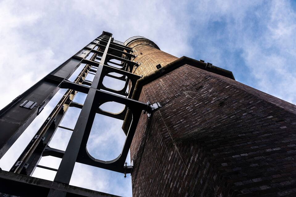 Una torre de maó alta amb una estructura metàl·lica i una finestra circular a la part superior.
