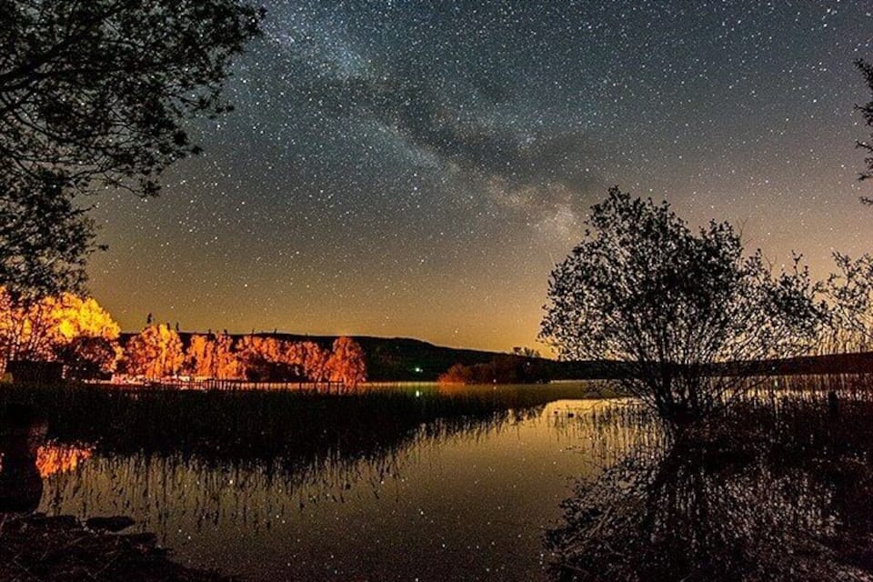 A starry night sky over a calm lake with trees reflecting the sky.