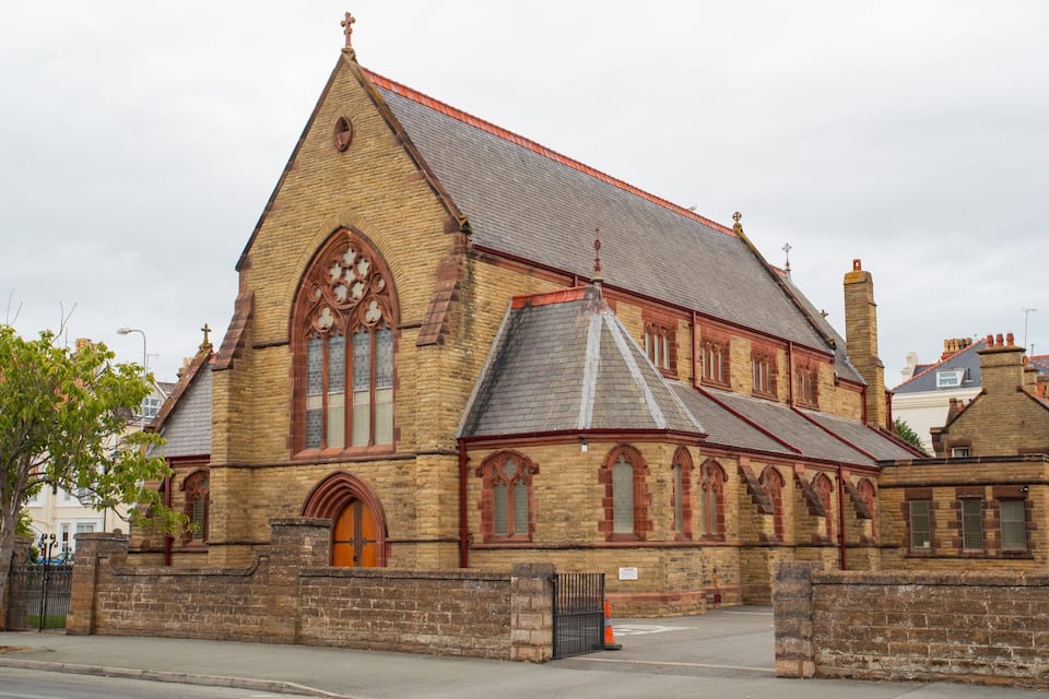 A historic church with a steeply pitched roof, large arched windows, and a brick facade.