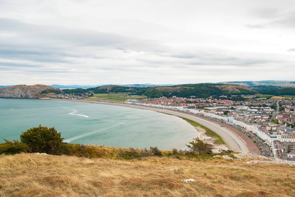 A coastal town with a beach, a winding road, and rolling hills in the background.