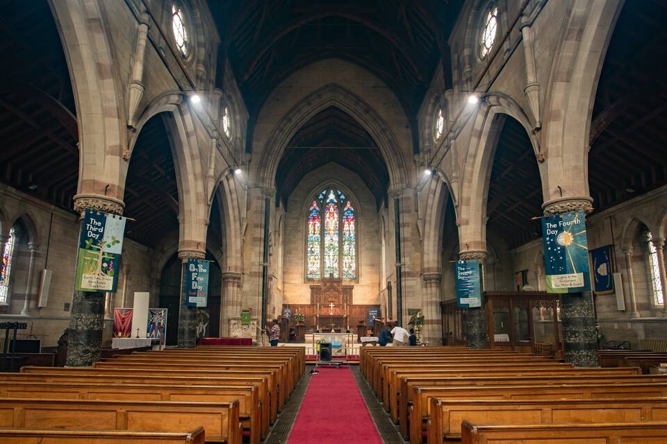 A church interior with wooden pews, stained glass windows, and banners.