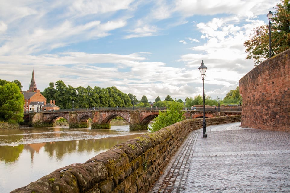 A stone bridge over a river, a brick wall, and a church with a spire.