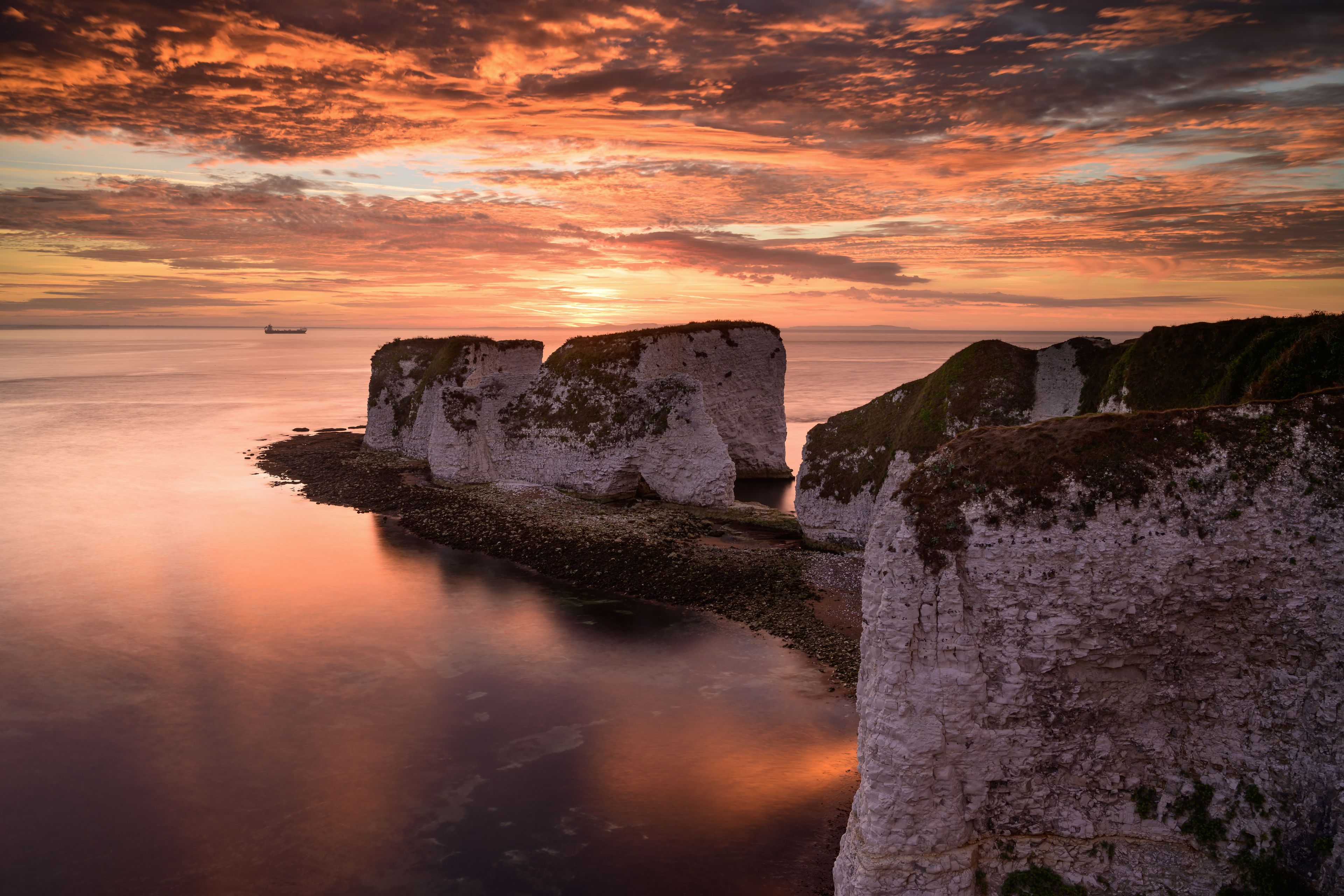 Un paisaje costero con acantilados blancos y aguas tranquilas que reflejan la puesta de sol.