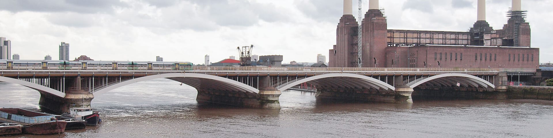 A bridge over a river with industrial buildings and smokestacks in the background.
