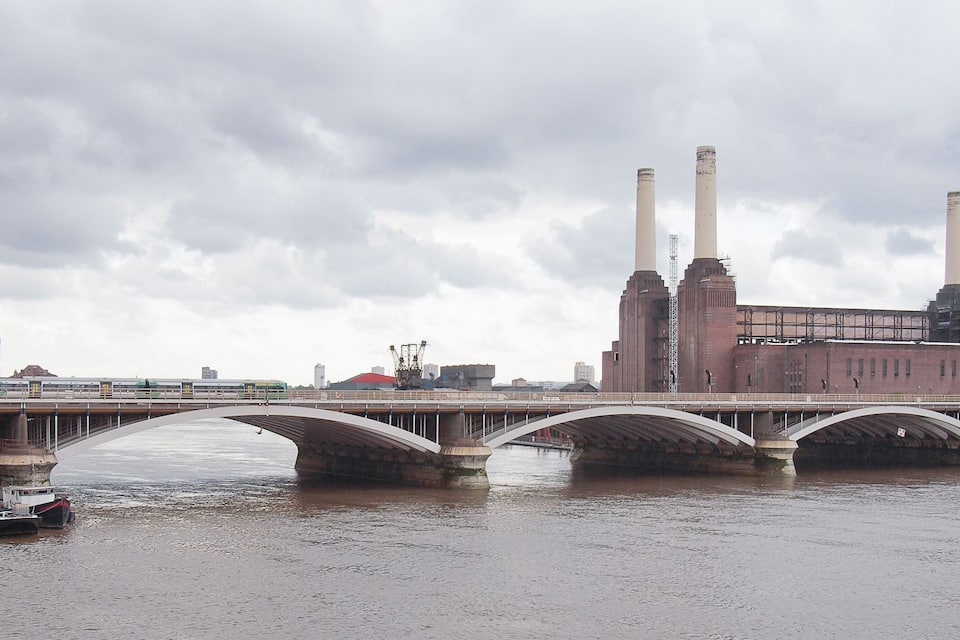A bridge over a river with industrial buildings and smokestacks in the background.