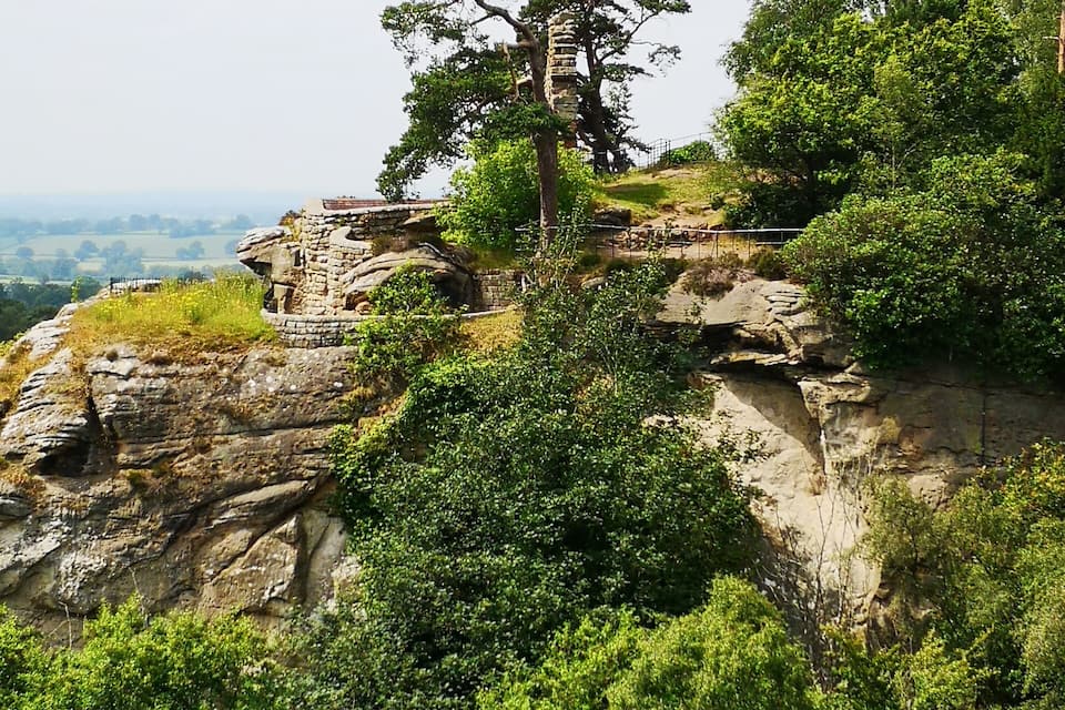 Une falaise rocheuse surmontée d’une construction en pierre et d’un arbre.