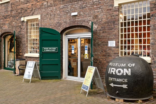 A museum entrance with a large stone marker labeled 'Museum of Iron' and directional signs.