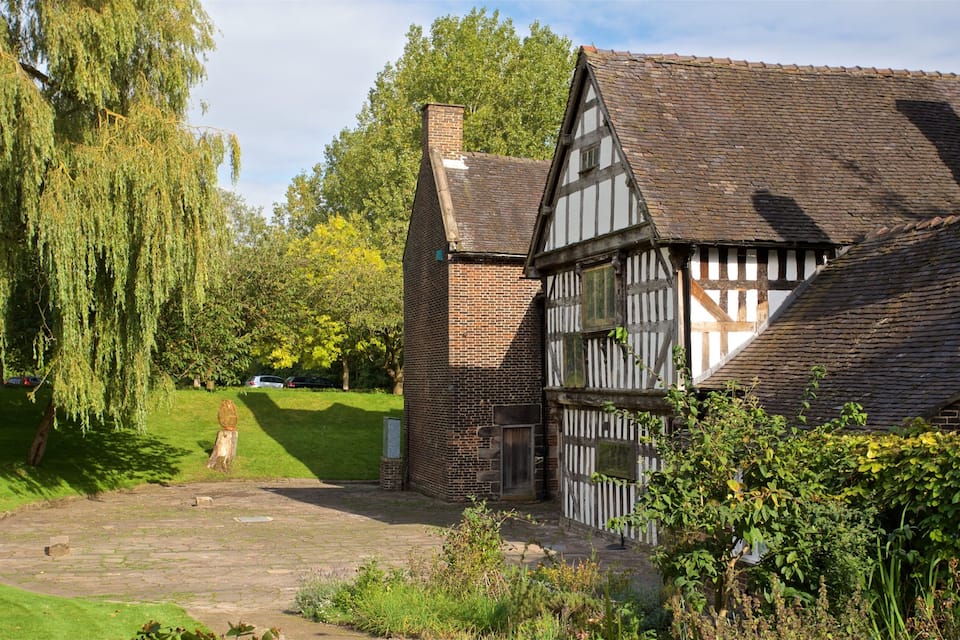 Uma casa em estilo Tudor com chaminé de tijolos, rodeada por vegetação exuberante e um caminho de pedra.