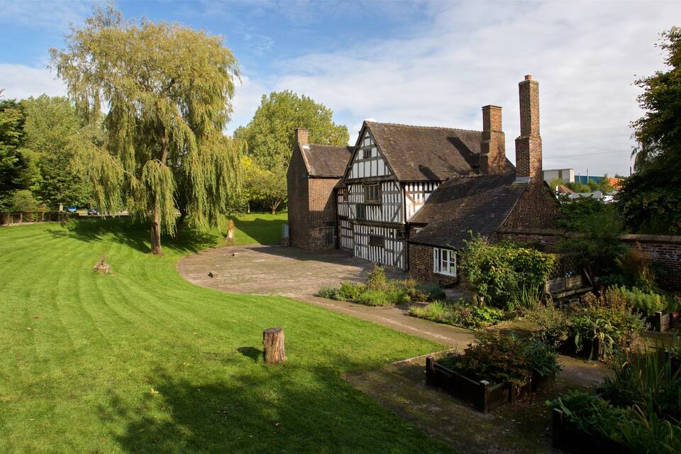 A Tudor-style house with a well-maintained lawn and a large tree in the foreground.