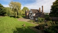 A Tudor-style house with a well-maintained lawn and a large tree in the foreground.