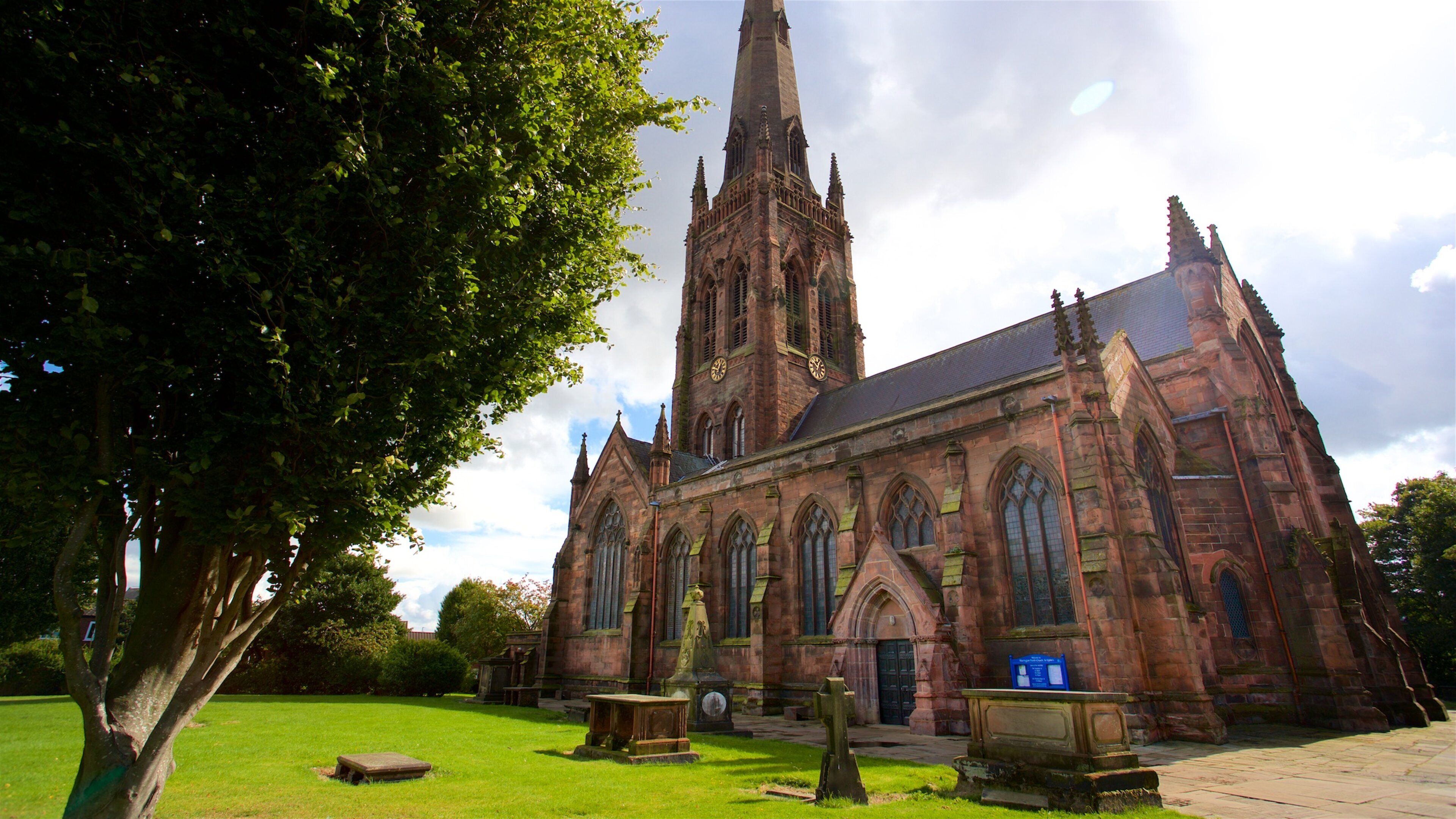 A large church with a tall spire, surrounded by a grassy area with a few trees.