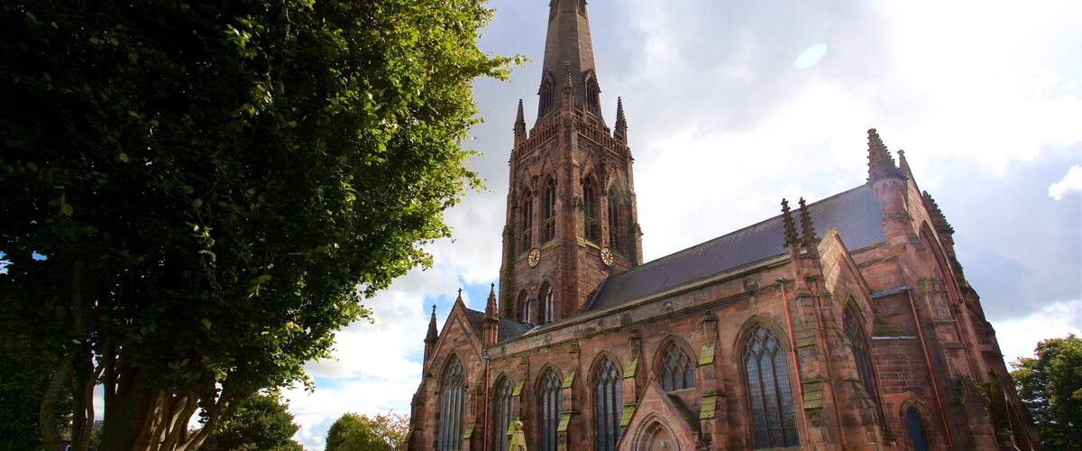 A large church with a tall spire, surrounded by a grassy area with a few trees.