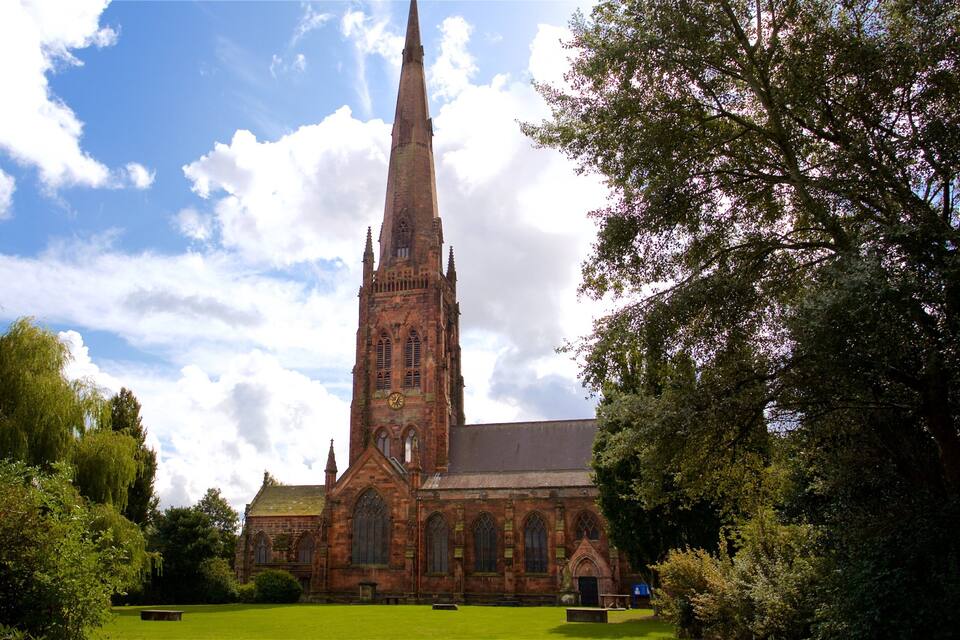 A historic church with a tall spire, surrounded by lush greenery and a clear blue sky.