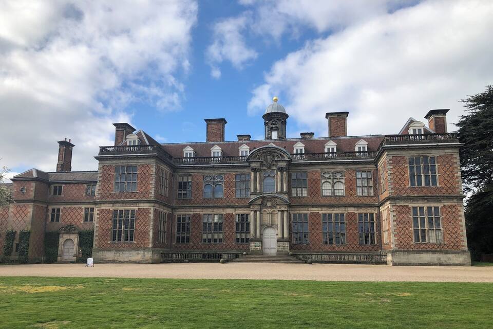 A large, historic building with a symmetrical facade, multiple chimneys, and a central entrance with a decorative arch.