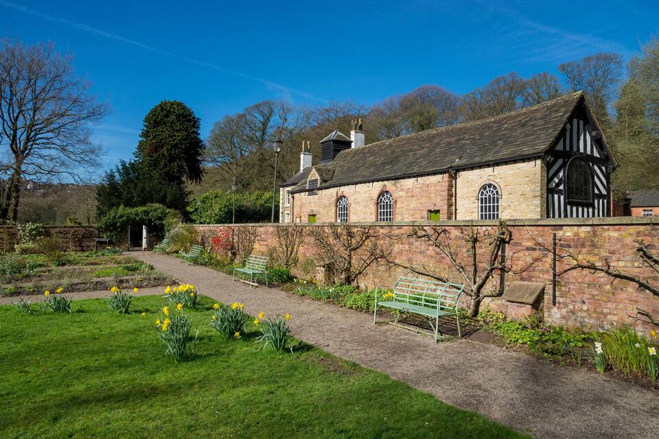A historic stone building with a garden path, benches, and blooming daffodils.