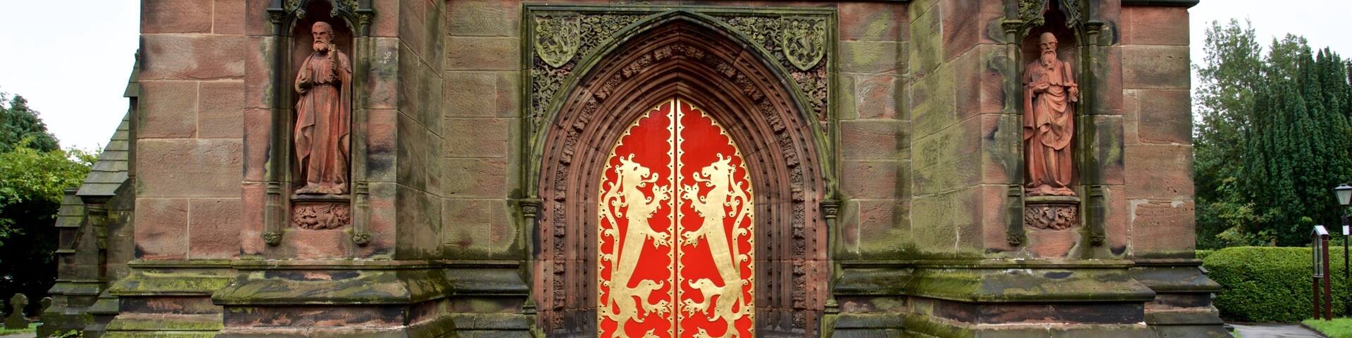 La entrada de una iglesia histórica con un vitral rojo y dorado, flanqueada por estatuas y elaboradas esculturas de piedra.