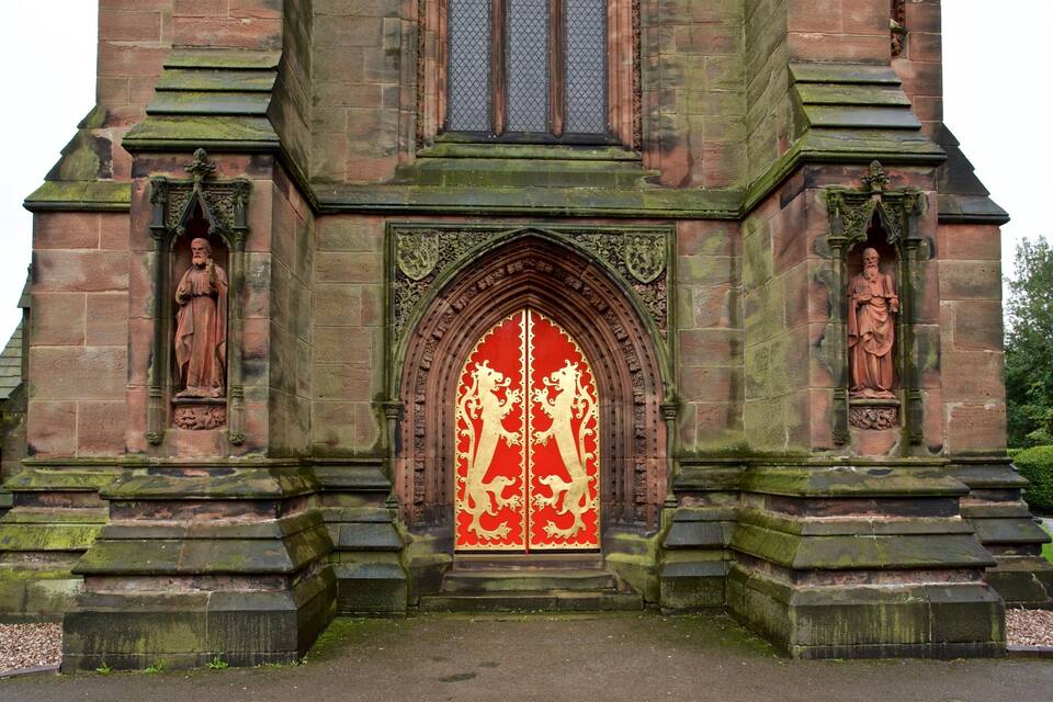 A historic church entrance with a red and gold stained glass window, flanked by statues and intricate stone carvings.