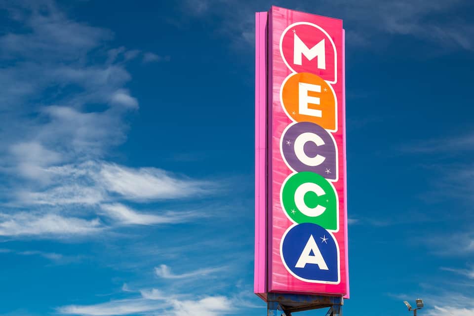 A vertical sign with the letters M, E, C, C, A against a blue sky.