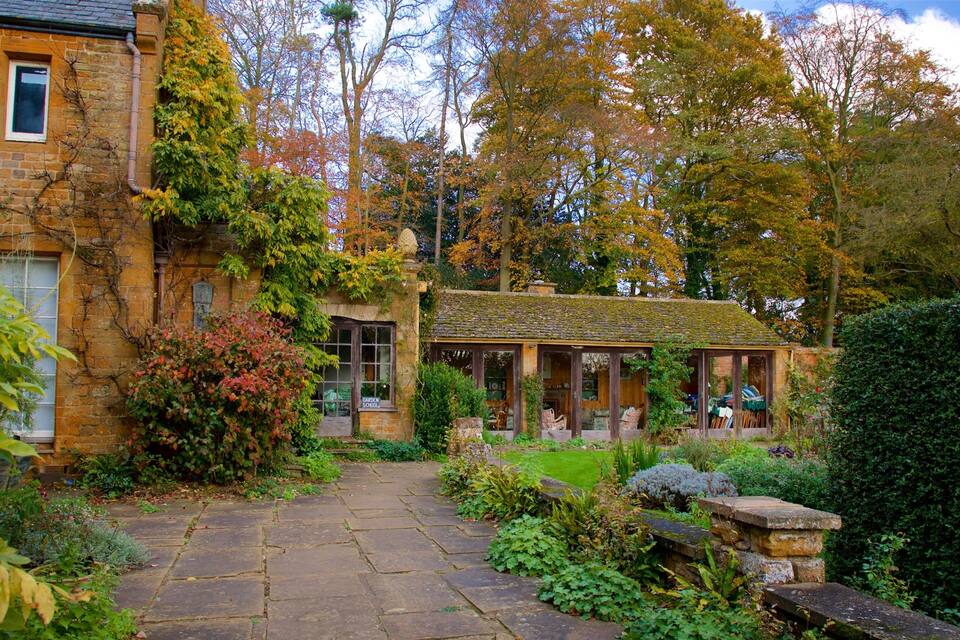 A stone house with a garden, surrounded by trees and a stone pathway.