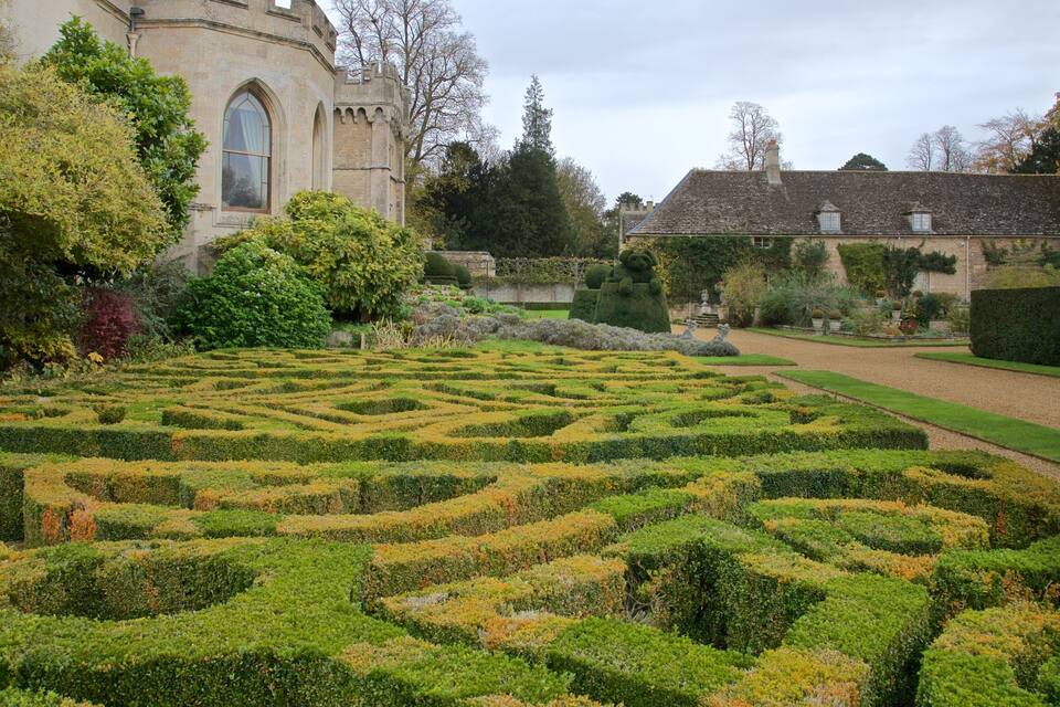 A formal garden with a hedge maze, a historic building, and a well-maintained lawn.