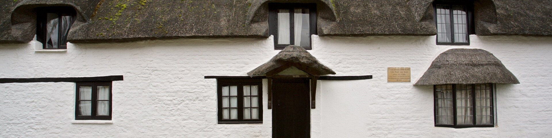 Um edifício branco com telhado de colmo, janelas com molduras pretas e chaminé de pedra.