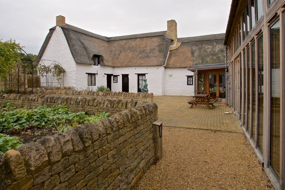 A white building with a thatched roof, stone walls, and a gravel courtyard.