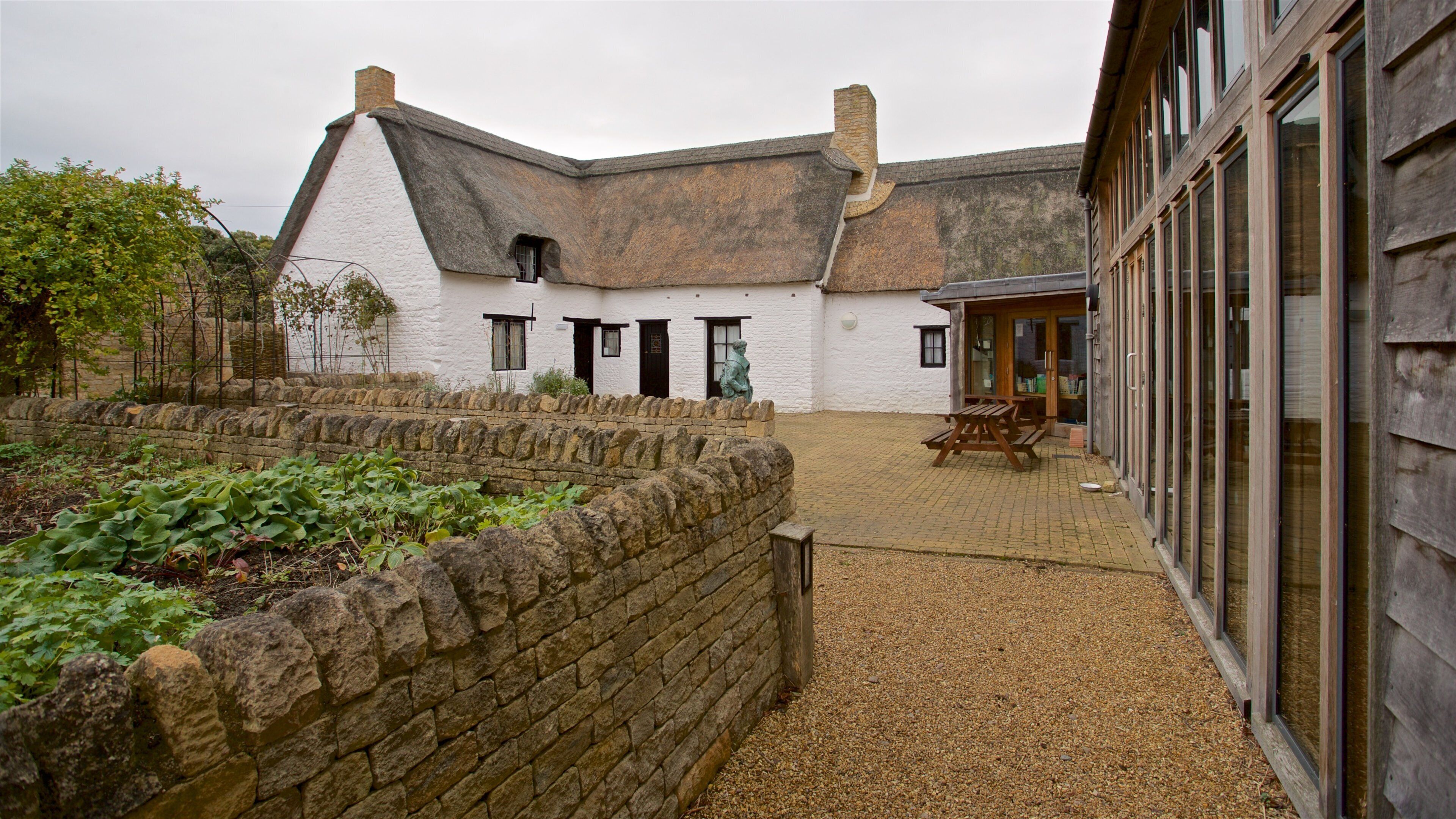 A white building with a thatched roof, stone walls, and a gravel courtyard.