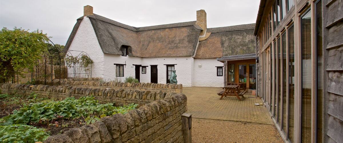 A white building with a thatched roof, stone walls, and a gravel courtyard.
