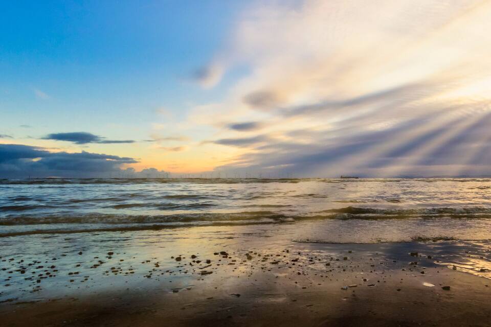 Ein Strand mit Wellen, Sonnenuntergang und bewölktem Himmel.
