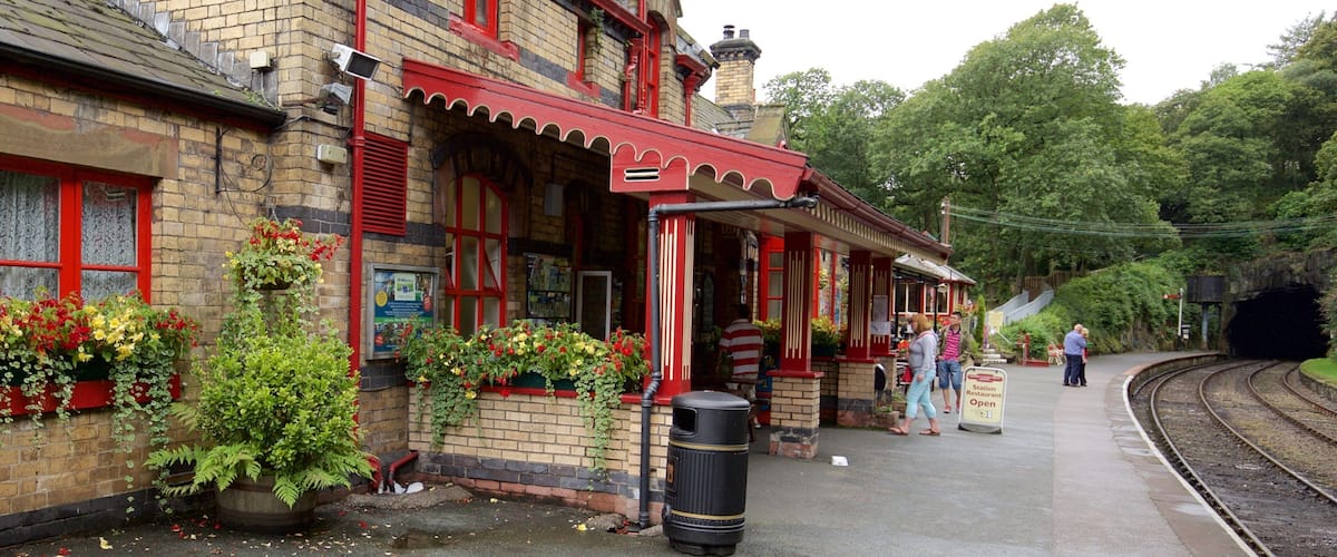 A historic train station with red brick architecture, flower boxes, and a platform with people.